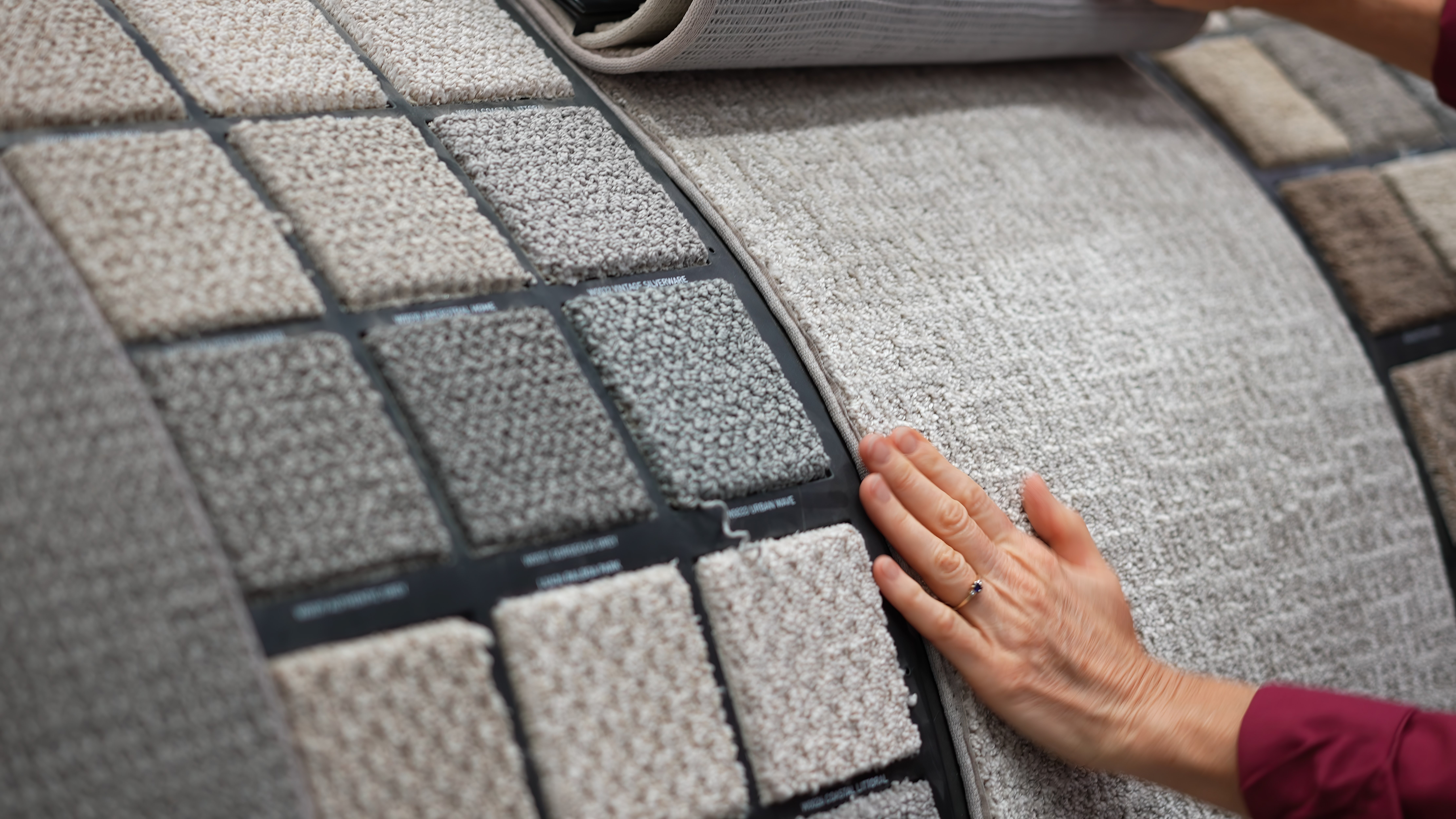 A woman runs her hand over carpet samples, shopping from carpet suppliers at a showroom.